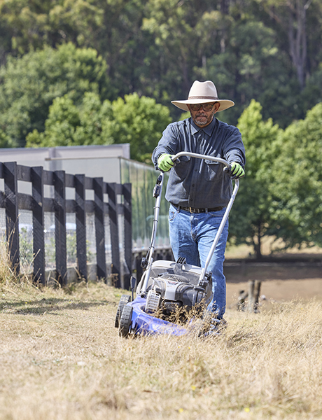 Man wearing hat mowing along a fence line